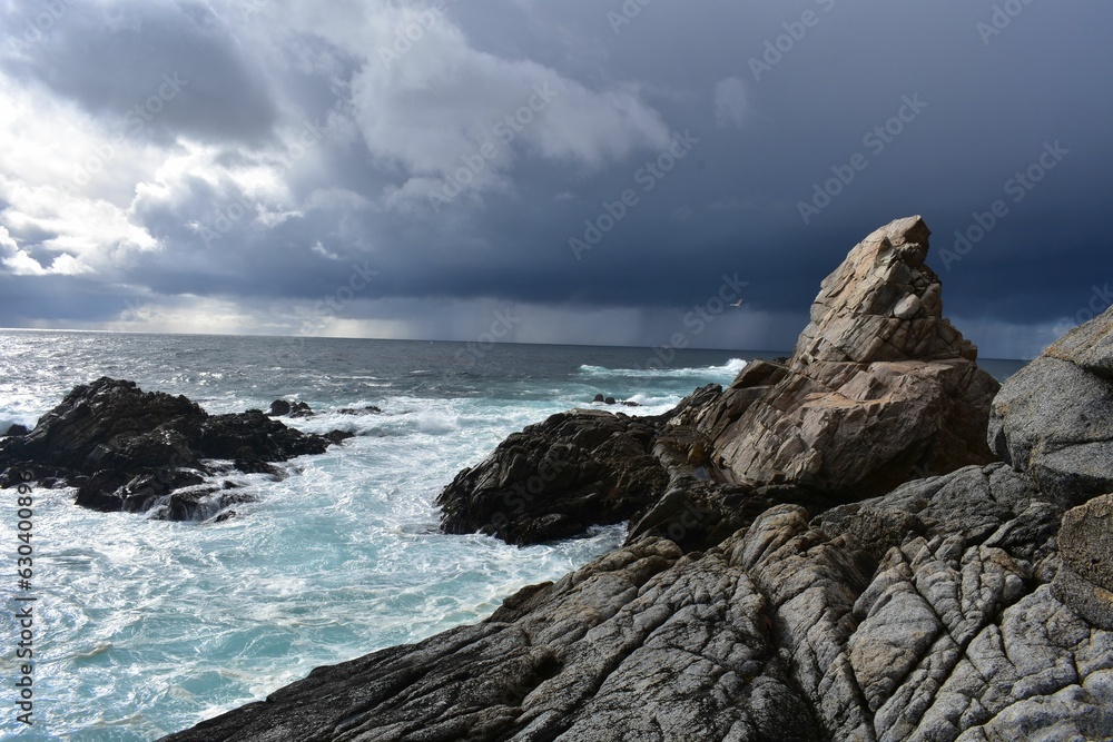 a rock formation with waves and a grey sky in the background