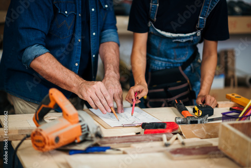 Small business furniture owner and professional architect interior designer working in carpenter workshop with blueprint and tablet discussing about home furnishing design project.