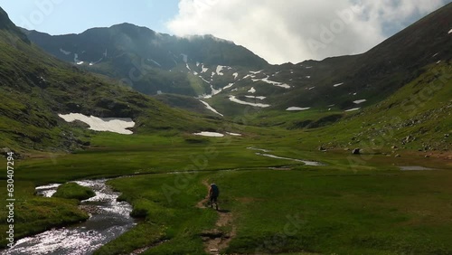 Hiker walking in the green field alongside the water stream with mountains in the background photo