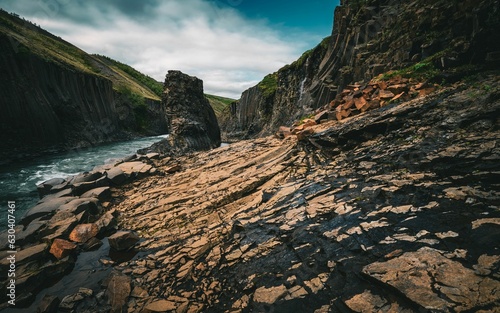 Expansive landscape of sun-drenched rocks on the edge of a serene river in Studlagil canyon, Iceland photo