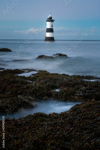 Penmon Point Lighthouse  in Anglesey standing on a rocky shoreline against a clouded sky