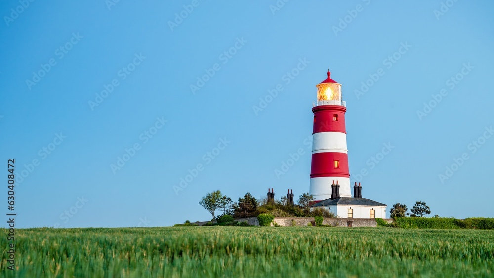 Majestic lighthouse with a vibrant red beacon in an expansive grassy field Majestic lighthouse with a vibrant red beacon in an expansive grassy field