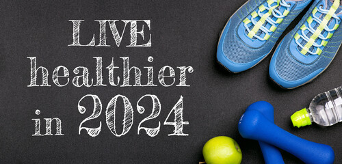 New year 2024 resolutions healthy lifestyle and sport. Be healthy in 2024. Motivation sport goals 2024 with sport equipment shoes, dumbbells, fruit and water bottle on black background