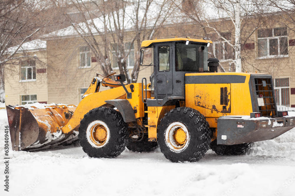 Orange tractor cleans up snow from the road and loads it into the truck. Cleaning and cleaning of roads in the city from snow in winter. Snow removal after snowfall and blizzards. Orange tractor cleans up snow from the road and loads it into the truck. Cleaning and cleaning of roads in the city from snow in winter. Snow removal after snowfall and blizzards.