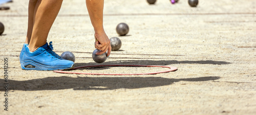 Hand of young sporty woman in sports shoes catching metal petanque ball to compete in qualifying game playing petanque game on a sunny day on a sandy ground petanque court photo