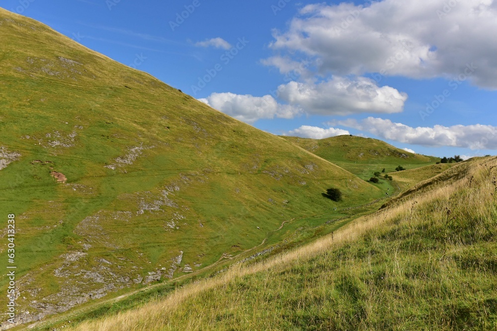 Scenic view of green hills under a cloudy blue sky on a sunny day