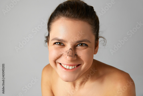 Pretty young woman with well-kept  healthy skin taking off nose mask after cleansing pores over grey studio background. Concept of natural beauty  cosmetology and dermatology  skincare  cosmetics  ad