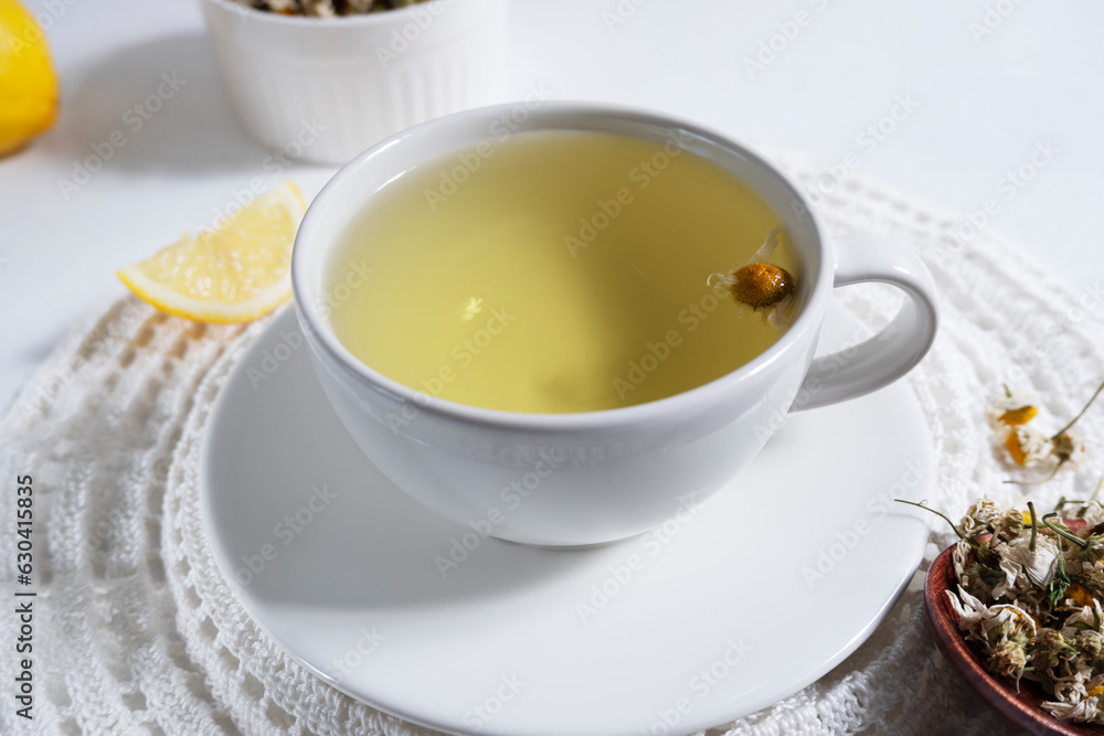 A decoction of chamomile brewed in a white cup on a white napkin on a light background. Medicinal decoction of chamomile, herbal tea. A decoction of chamomile brewed in a white cup on a white napkin on a light background. Medicinal decoction of chamomile, herbal tea.