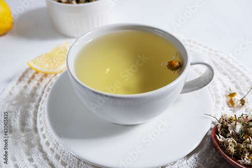A decoction of chamomile brewed in a white cup on a white napkin on a light background. Medicinal decoction of chamomile, herbal tea.