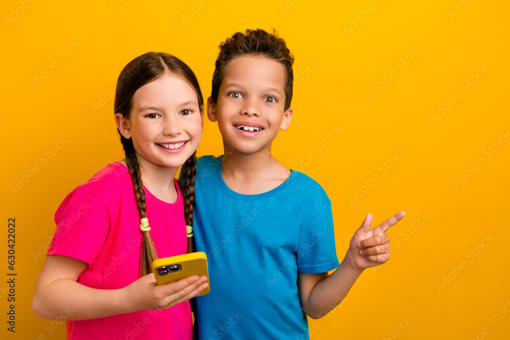 Photo of funky sweet preteen schoolchildren wear t-shirts chatting apple samsung iphone device empty space isolated yellow color background Photo of funky sweet preteen schoolchildren wear t-shirts chatting apple samsung iphone device empty space isolated yellow color background
