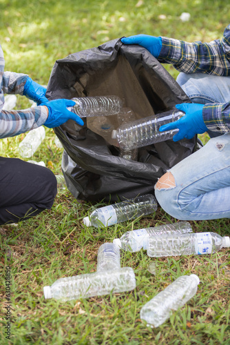 Two man employees use black garbage bags to collect plastic bottles and recyclable waste from the lawn and sidewalks for recycling. Concept of sorting plastic waste for recycling