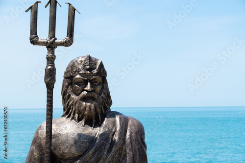 Statue of the god of the seas with a trident on the embankment against the background of the blue sea