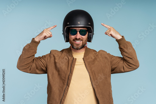 Portrait of handsome smiling bearded man, biker pointing fingers on helmet