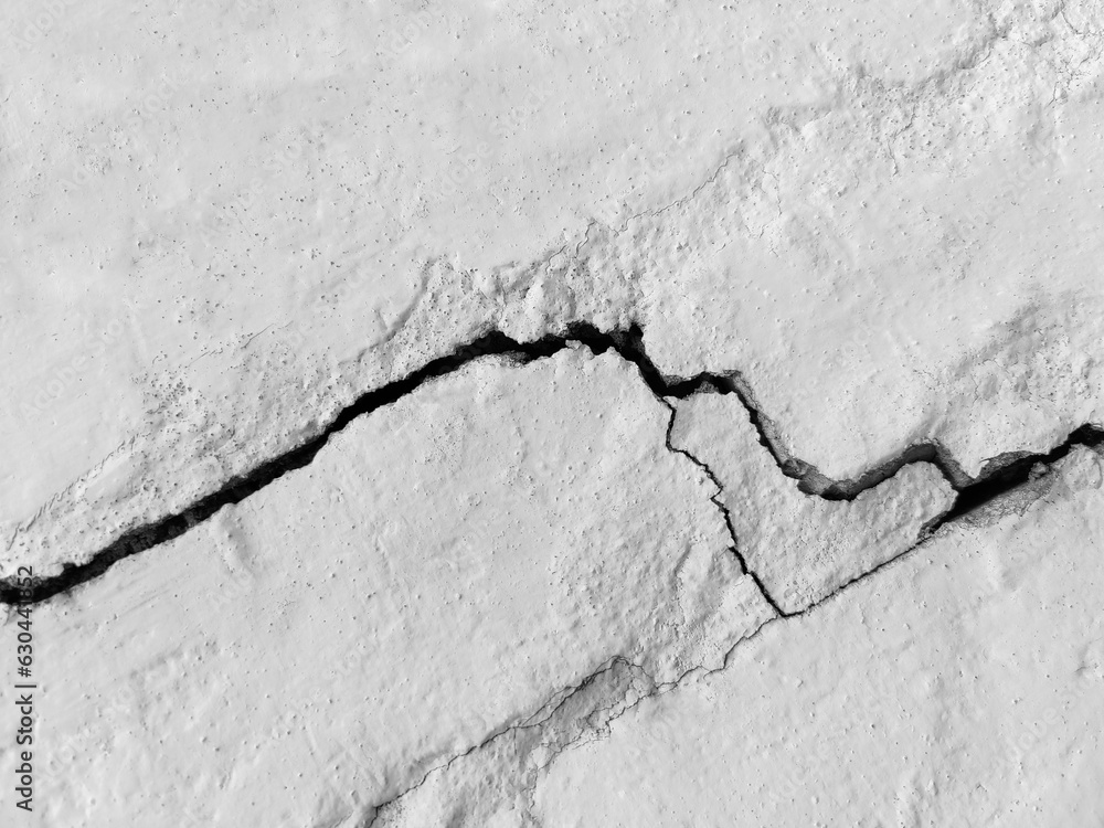 Obraz premium Big long tortuous crack on old plastering wall. Copy space. Black and white photo. Selective focus.