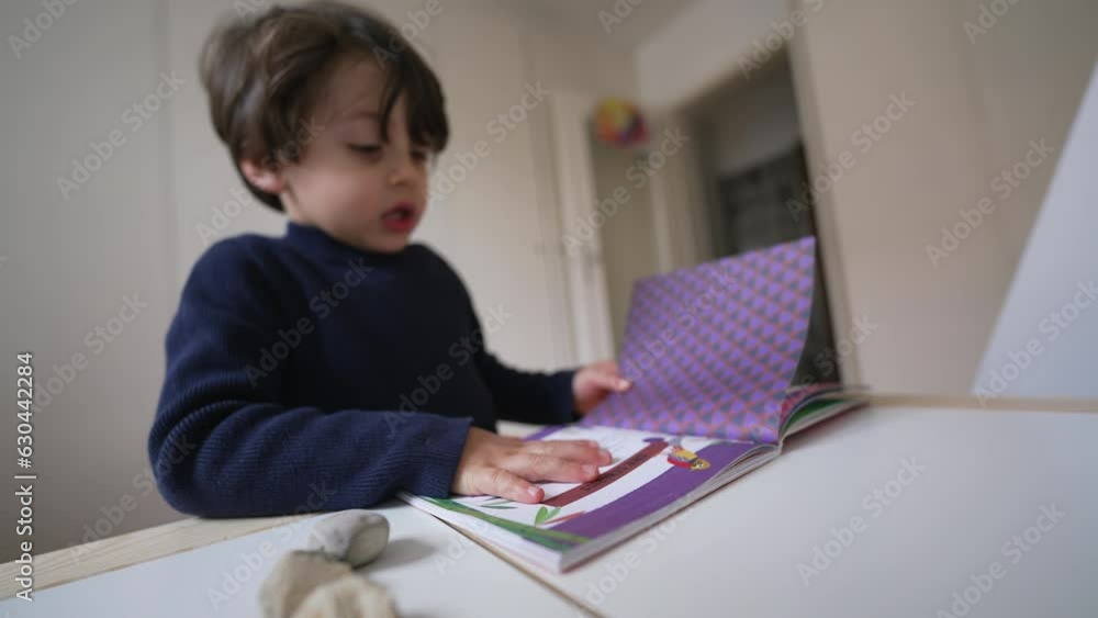 Child turning book pages looking at images and text. Little boy reading kindergarten school material Child turning book pages looking at images and text. Little boy reading kindergarten school material