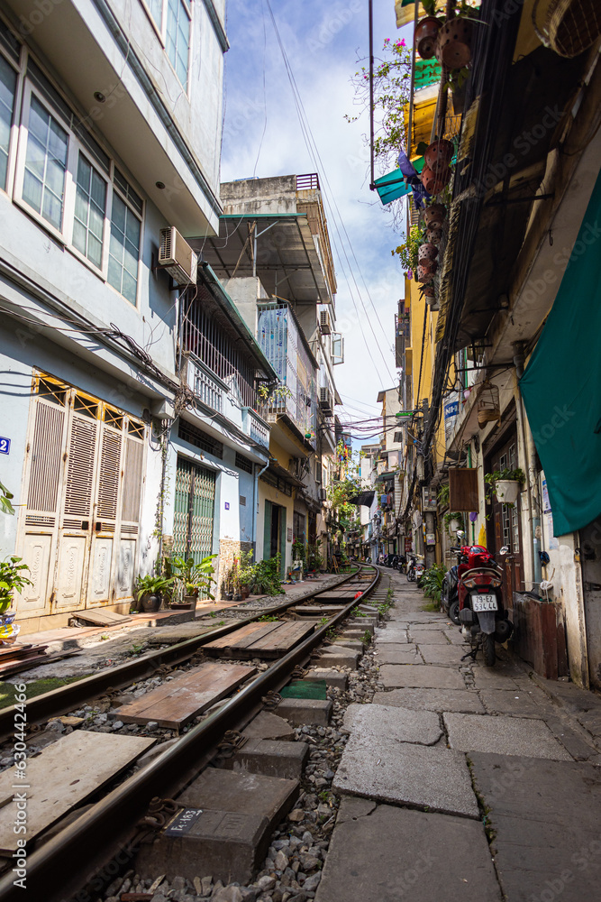 Obraz premium Hanoi, Vietnam - May 28, 2023: Train Street in Hanoi is a narrow, bustling lane with tracks. Close knit houses, adorned with plants, are inches away from passing trains. bars and cafes line the track
