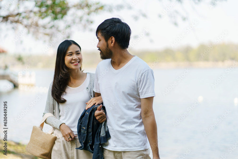Asian couple walking in garden with picnic basket. in love couple is enjoying picnic time in park outdoors Asian couple walking in garden with picnic basket. in love couple is enjoying picnic time in park outdoors