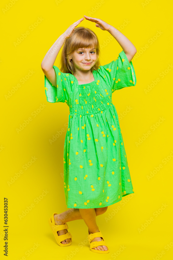 Young blonde child girl kid playing childish catching up game, feeling in safe making roof above head with hands, insurance, security service. Little preteen children on yellow background. Vertical Young blonde child girl kid playing childish catching up game, feeling in safe making roof above head with hands, insurance, security service. Little preteen children on yellow background. Vertical