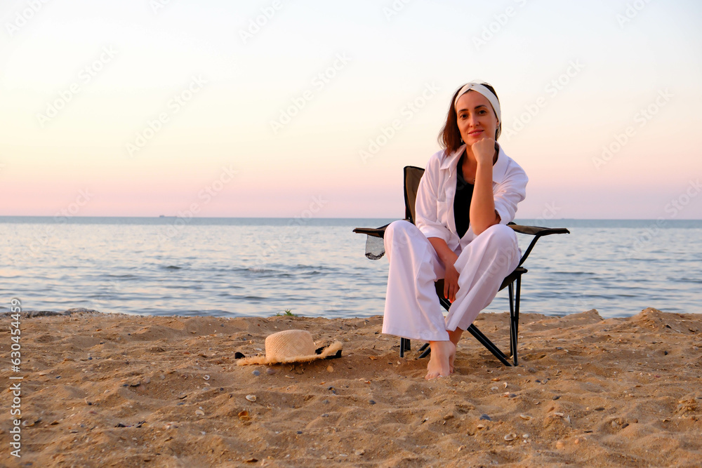 Beautiful cute woman in white suit and hat is sitting and relaxing on sea beach coastline. Beautiful cute woman in white suit and hat is sitting and relaxing on sea beach coastline.