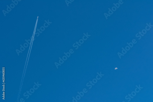 Blue clear sky with a flying airplane and a half-full moon