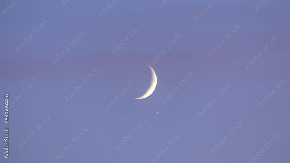 Blue sky and slowly moving pink clouds, crescent Moon and the light of the planet Jupiter. The conjunction of Jupiter with the Moon observed in October 2019.