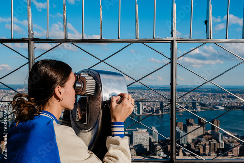 young girl looking at view of manhattan skyline with binoculars from the Empire State Building