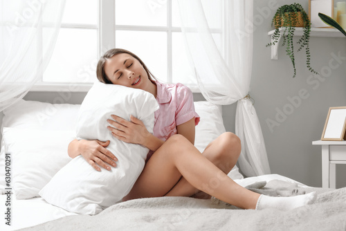 Pretty young woman with soft pillow sitting on bed