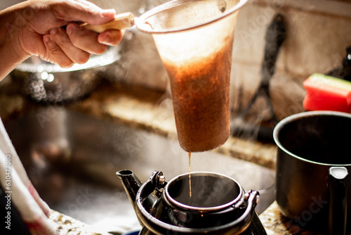 Mão coando café em um coador de pano em uma cozinha rústica, transmitindo a simplicidade e o sabor autêntico do café feito na hora. photo