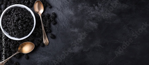 The top view of a bowl with delicious black caviar and a vintage silver spoon is shown on a dark concrete background with empty space for text.