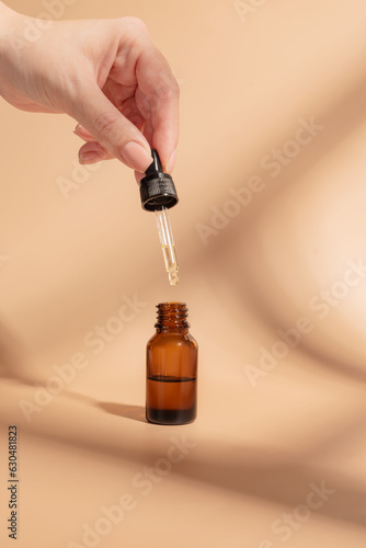 female hand with Dropper of essential oil, aromatherapy essence, beuty serum or medicinal liquid on beige background. Unbranded bottles for your design.