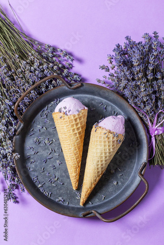 Obraz na płótnie Two lavender ice creams in waffle cones on a tin tray and bouquets of dry lavender on a lilac background. w salonie