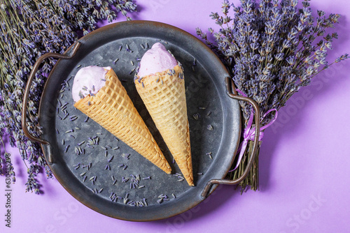 Obraz na płótnie Two lavender ice creams in waffle cones on a tin tray and bouquets of dry lavender on a lilac background. w salonie
