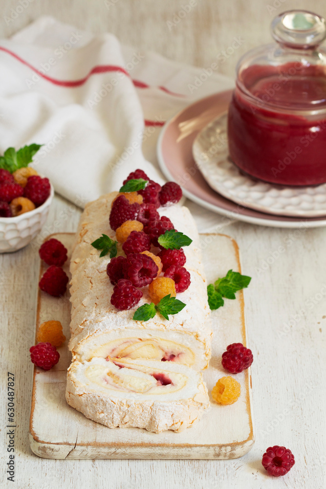 Meringue roll with butter cream and raspberry curd, decorated with berries on a light background.