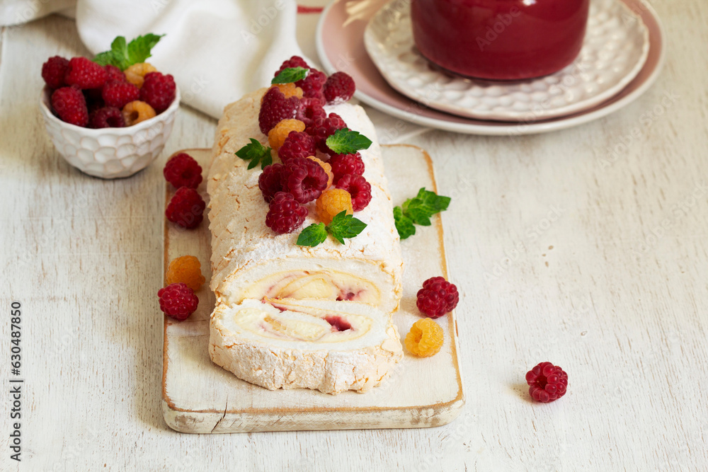 Meringue roll with butter cream and raspberry curd, decorated with berries on a light background.