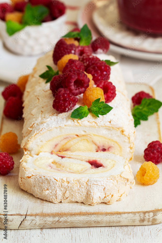 Meringue roll with butter cream and raspberry curd, decorated with berries on a light background.