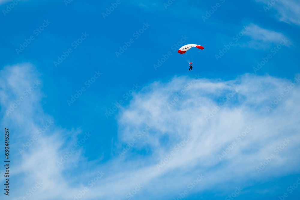 Parachutist with a white and red parachute against the blue sky Parachutist with a white and red parachute against the blue sky