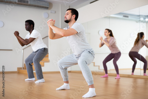 Group of people squatting during fitness training in studio.