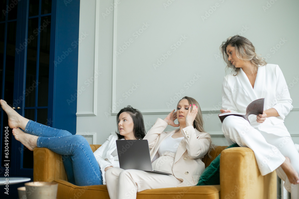 Three business ladies sitting on sofa, pregnant woman and blonde with journal looking at monitor, brunette distracted. Three business ladies sitting on sofa, pregnant woman and blonde with journal looking at monitor, brunette distracted.
