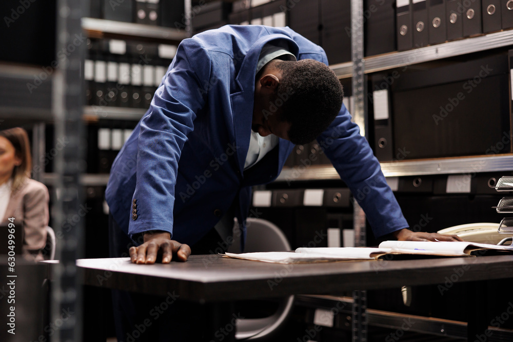 Thoughtful detective working in arhive room, analyzing crime scene evidence late at night in arhive room. Private investigation checking victim report searching for mysterious suspect files Thoughtful detective working in arhive room, analyzing crime scene evidence late at night in arhive room. Private investigation checking victim report searching for mysterious suspect files