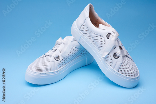 Comfortable women's white sneakers from perforated leather with white rubber sole on the gradient blue background. Concept of the sport casual footwear