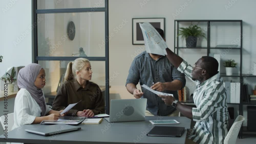 Group of multi-ethnic managers sitting at table in office refusing to listen to their colleague and offending him during meeting Group of multi-ethnic managers sitting at table in office refusing to listen to their colleague and offending him during meeting