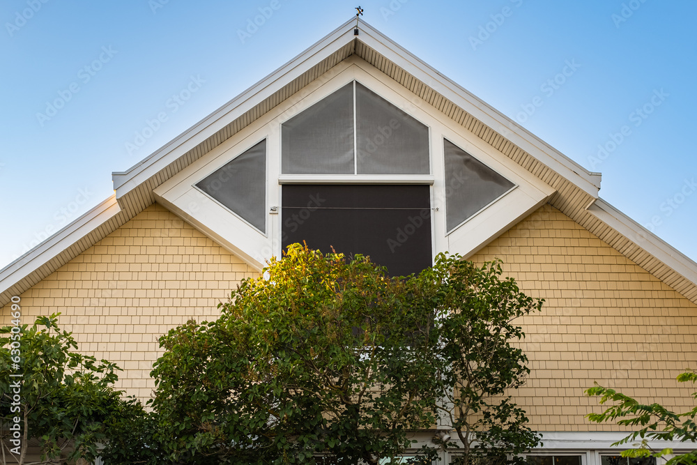 Top of the triangular roof of the house against the sky. Exterior Front House Facade. Top of the house with windows Top of the triangular roof of the house against the sky. Exterior Front House Facade. Top of the house with windows