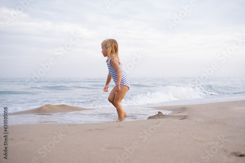 Little girl with long hair running looking at sea waiting on sandy beach at Mediterranean seaside in Spain. Carefree childhood  freedom  happiness concept.