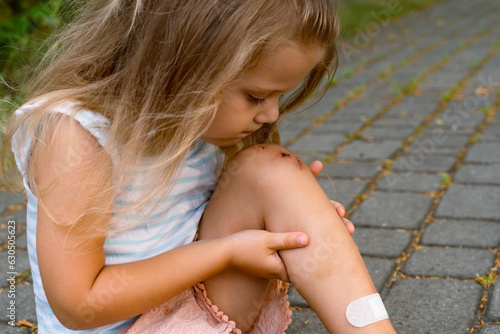 A little girl puts a band-aid on a wound on her knee after an accident. Selective focus. photo