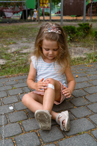 A little girl puts a band-aid on a wound on her knee after an accident. Selective focus.