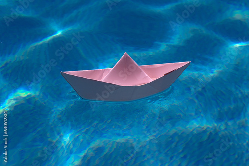 Paper boat sailing on water causing waves and ripples. Paper boat into water. Concept of tourism, travel dreams vacation holiday, dreaming traveling, sailing adventure. Paper craft and origami. © Volodymyr