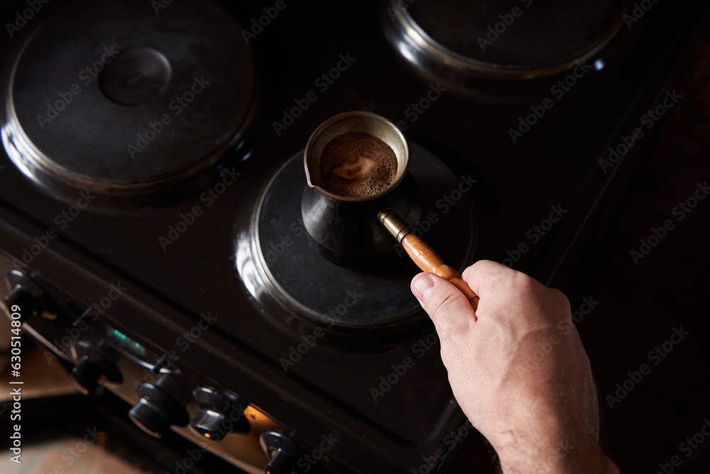 A man preparing black coffee on electric stove. Brew coffee in a Turkish coffee pot A man preparing black coffee on electric stove. Brew coffee in a Turkish coffee pot