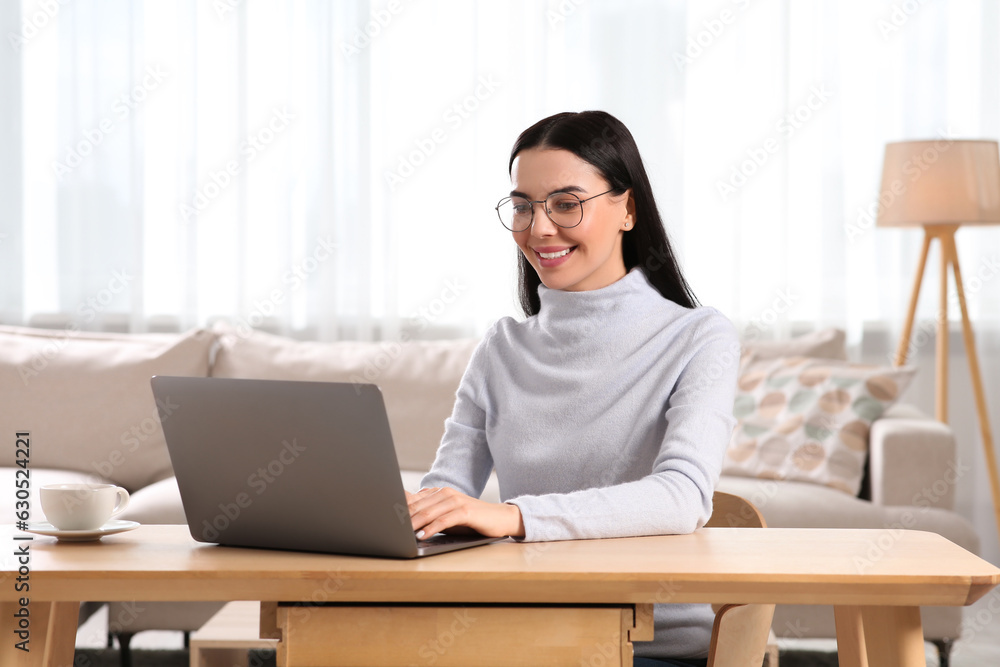 Happy woman working with laptop at wooden desk in room Happy woman working with laptop at wooden desk in room
