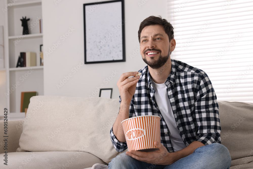 Happy man watching TV while eating popcorn on sofa at home Happy man watching TV while eating popcorn on sofa at home