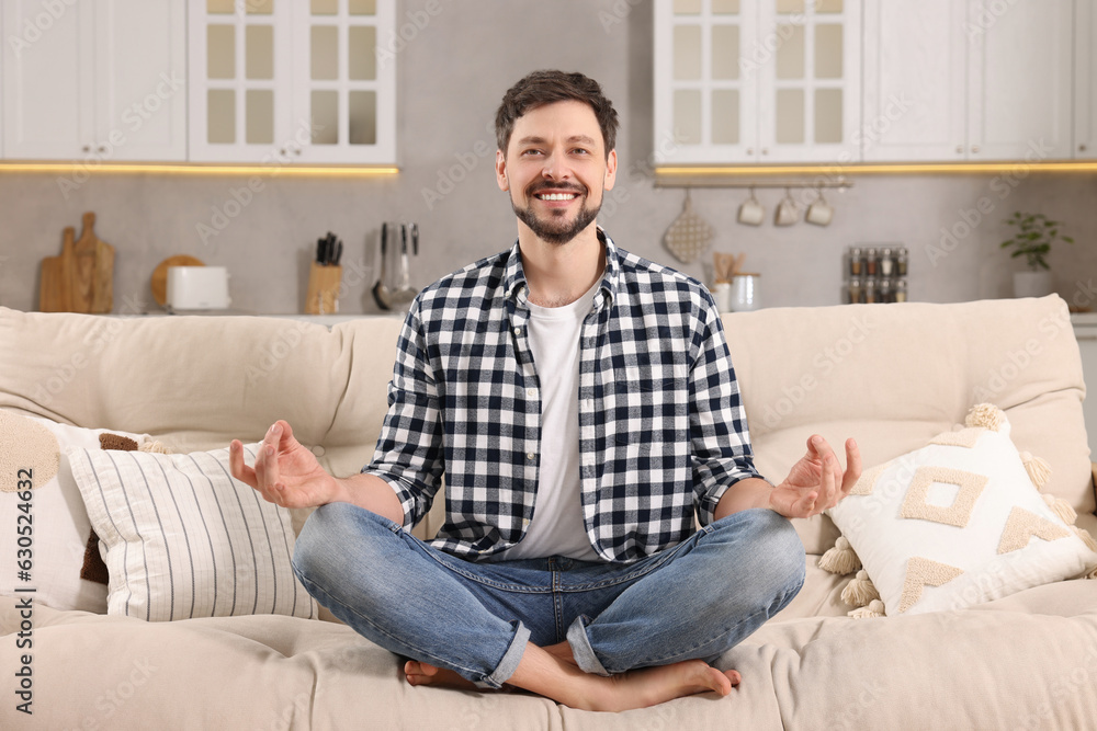Happy man meditating on sofa at home. Harmony and zen